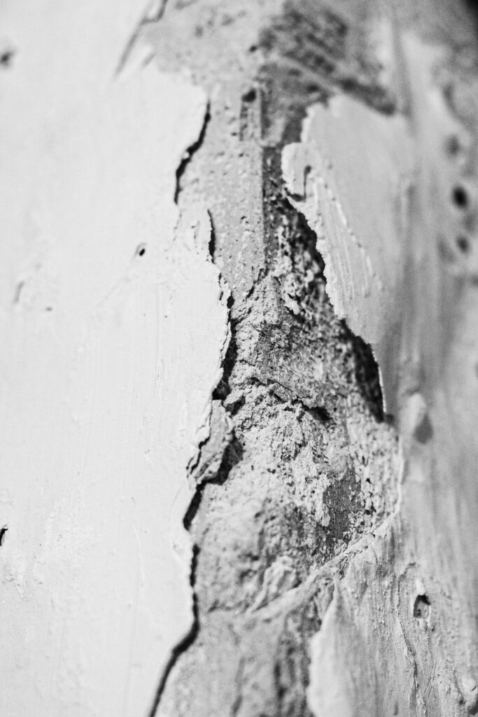 Close-up van beschadigde voeg in wit plafondelement met afbrokkeling en losse stofdeeltjes
